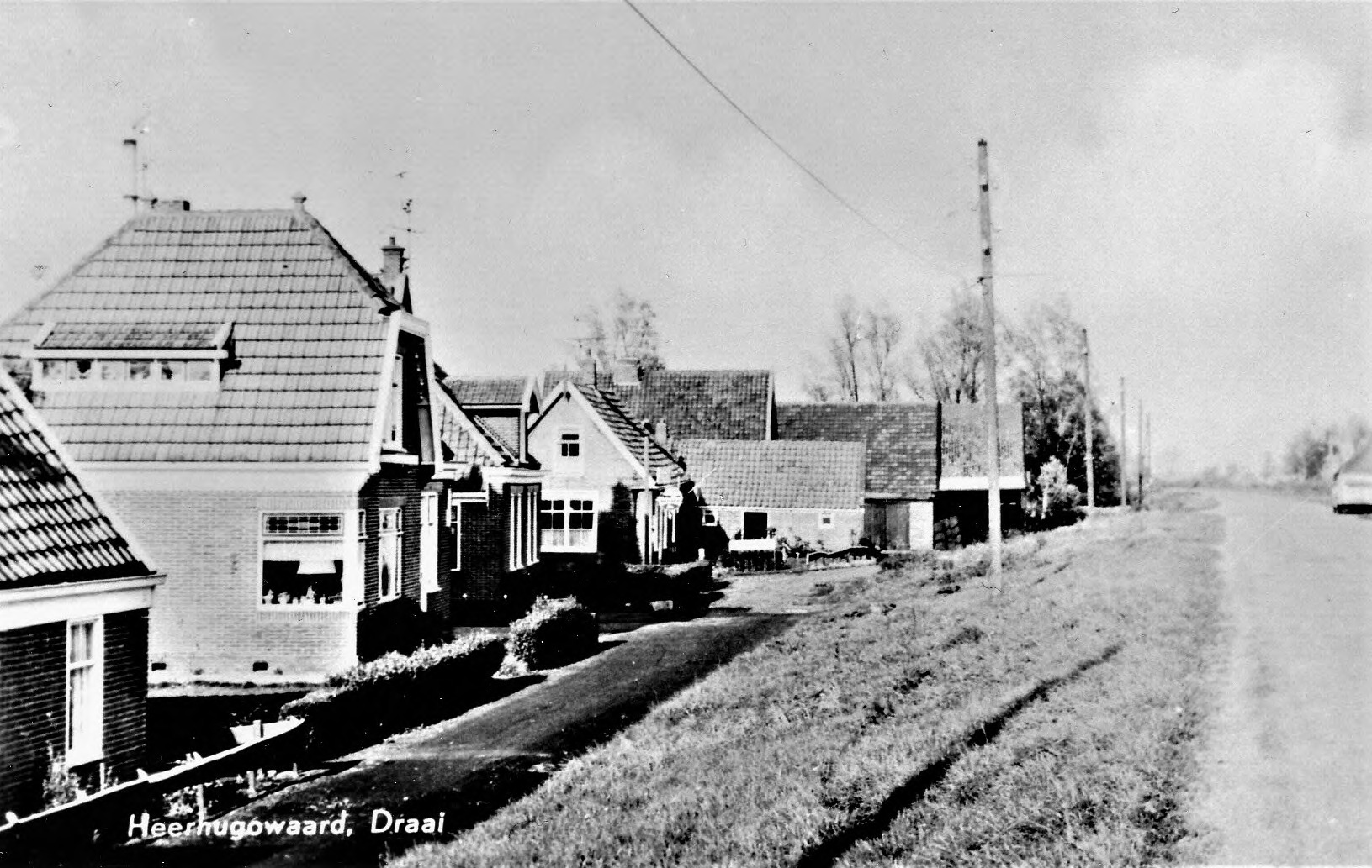 Zwart-witfoto van de Oostdijk: woningen en een houten schuur langs de dijk